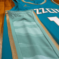 Regata City Edition Charlotte Hornets Jordan 2023/24 Azul e Dourada - Inspirada na história dourada de Charlotte, com design azul-petróleo, detalhes em menta e dourado. Logotipos primários em ouro, branco e azul. Painéis laterais menta lembrando uma colmeia, emblema de vespas douradas nos shorts e a frase "The Hive is Alive" no jocktag.